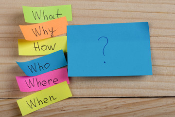 Questions - Why? What? Where? When? Why? How? on colorful stickers on wooden desk