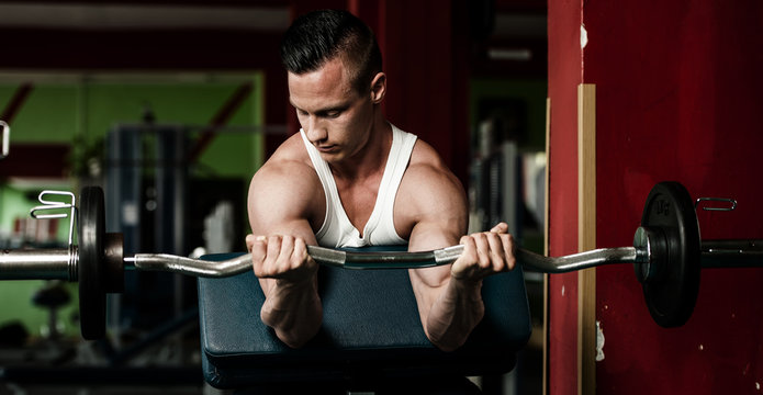 phisique fitness competitor works out in gym lifting dumbbells