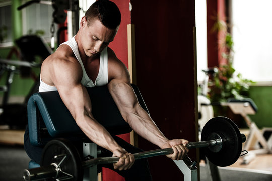 phisique fitness competitor works out in gym lifting dumbbells