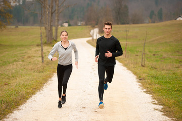 Young  veautiful couple runs on a path in park on autumn afternoon