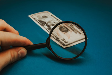 fifty dollar bill on a blue background being studied through a magnifying glass.