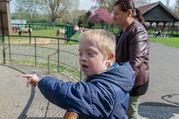 Obraz premium Defect,childcare,medicine and people concept: Happy mother and son with down syndrome playing together in a park at spring time.