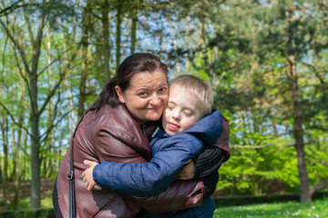 Defect,childcare,medicine and people concept: Happy mother and son with down syndrome playing together in a park at spring time.