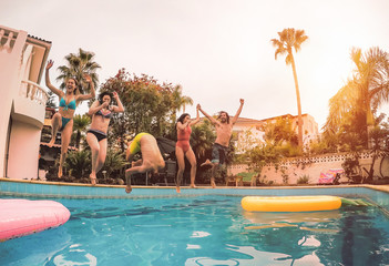 Group of happy friends jumping in pool at sunset time - Millennial young people having fun making...