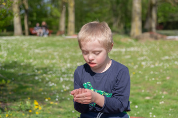   Defect,childcare,medicine and people concept: Blond boy with down syndrome playing in a park at spring time.