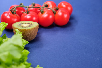 fresh vegetables and fruits on dark blue background. Lettuce, cherry tomatoes, half lemon and kiwi
