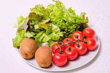 kiwis, lettuce and cherry tomatoes on a white plate on a white background