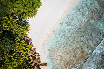 Girl sunbathing on tropical cocos beach with beautiful rocks, palm trees and ocean waves. Aerial drone shot. Seychelles