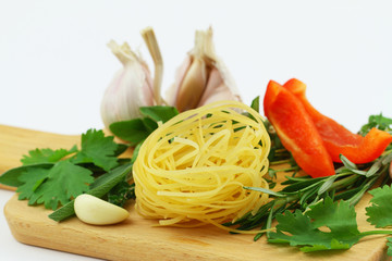 Closeup of uncooked tagliatelle, fresh herbs, garlic and red pepper on wooden surface