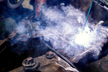 Close up industrial worker is welding repair auto in factory. Place for text.