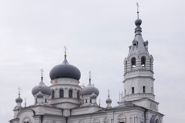 Obraz premium Christian orthodox white church with silver and grey domes with gold crosses. Calm grey sky above