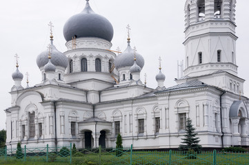 Christian orthodox white church with silver and grey domes with gold crosses. Calm grey sky above