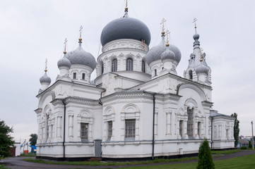 Christian orthodox white church with silver and grey domes with gold crosses. Calm grey sky above