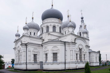 Fototapeta na wymiar Christian orthodox white church with silver and grey domes with gold crosses. Calm grey sky above