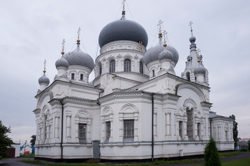 Fototapeta na wymiar Christian orthodox white church with silver and grey domes with gold crosses. Calm grey sky above
