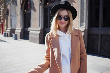 Fototapeta premium Happy girl outdoors, Sunny day. Fashionable and trendy young woman in black felt hat and stylish beige coat