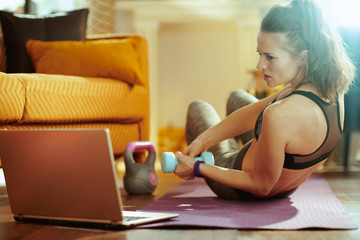 woman using online fitness site in laptop and doing exercises
