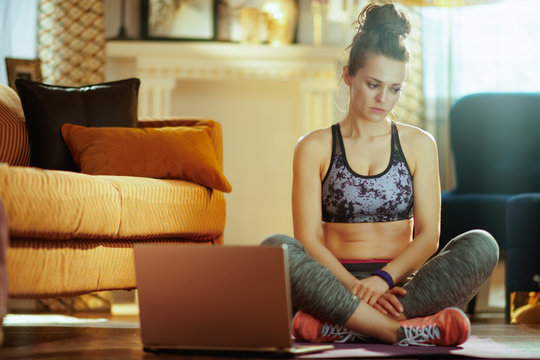 stressed fit sports woman with laptop sitting on fitness mat