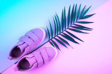 Sneakers and sprig of palm trees on a trendy color background, top view, summer shoes.