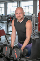 Fototapeta na wymiar handsome young man in blue shorts and black t-shirts, doing exercises for biceps in the gym. bald man smiling at camera