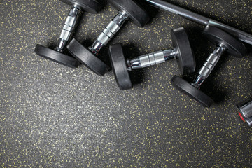 Many dumbbells lie randomly on the floor. Loft gym. Place for the text. Black wall.