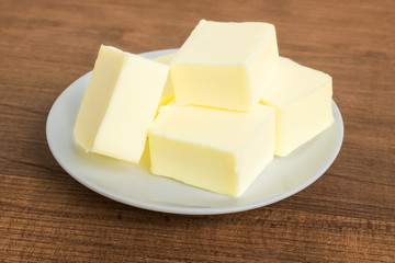 Close-up of fresh butter pieces on a white plate. Plate with butter on a brown wooden background. Sandwich butter. Natural fat nutrient.
