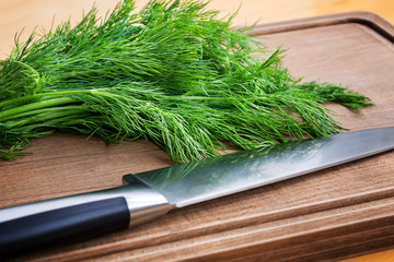 Close-up of fresh green dill and sharp professional chef knife on a brown wooden cutting board. Fresh greens for a healthy eating.