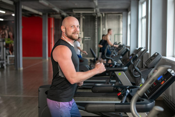 Fototapeta na wymiar Fit Muscle bald Man With Headphones Running on Treadmill in Gym. bald.man smiling at camera