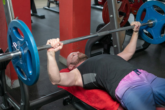 bald Weightlifter in the black t-shirt at the bench press lifting a barbell on an incline bench