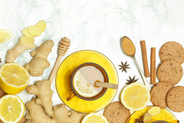 Ginger tea in a cup with ginger roots and lemon on marble textured background, top view. A healthy lifestyle, anti-flu and anti-inflammatory concept.