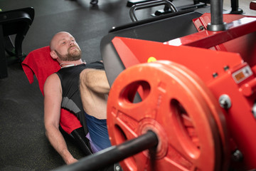 Side view of bald man in black t-shirt weightlifter doing leg presses in gym