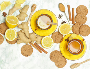 Ginger tea in a cup with ginger roots and lemon on marble textured background, top view. A healthy lifestyle, anti-flu and anti-inflammatory concept.