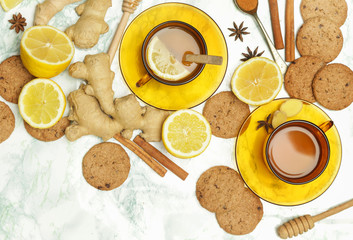 Ginger tea in a cup with ginger roots and lemon on marble textured background, top view. A healthy lifestyle, anti-flu and anti-inflammatory concept.