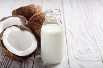 Milk or yogurt in glass bottle on white wooden table with coconut aside