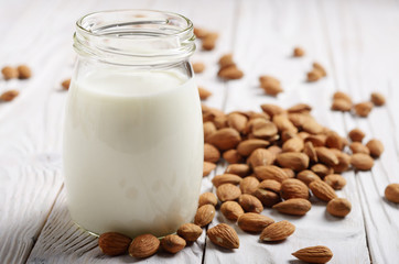 Obraz na płótnie Canvas Milk or yogurt in mason jar on white wooden table with almonds aside