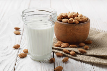 Obraz na płótnie Canvas Milk or yogurt in mason jar on white wooden table with bowl of almonds on hemp napkin aside
