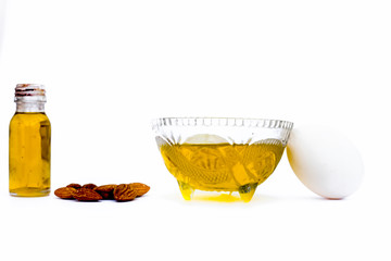 Home remedy to cure hair damage isolated on white i.e. almond oil along with egg white well mixed in a glass bowl and all the raw ingredients present on the surface.