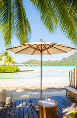 White umbrella on wooden decking with summer view of sunny beach of Bora Bora island