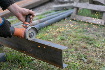 a welder in blue jeans and black boots is sawing a metal profile with a Bulgarian sparks are flying