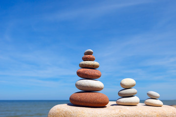 Fototapeta na wymiar Three Zen pyramid of balanced stones on a background of the summer sea and blue sky
