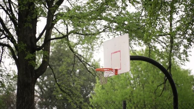 Basketball hoop in urban neighborhood park while rain falls in super slow motion