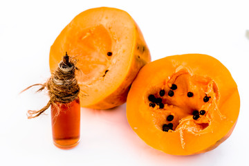 Raw cut papaya isolated on white along with its concentration or essence in a transparent glass bottle.