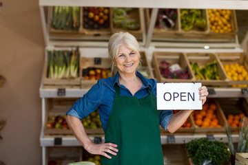 Senior woman holding open sign in organic produce shop