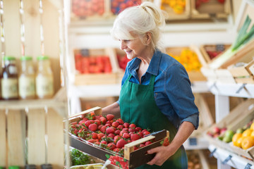 Shop assistant holding box with fresh strawberries in organic produce shop