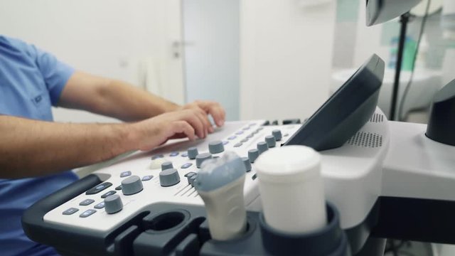 Close up hands of doctor presses buttons and works on ultrasound device. 