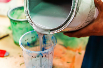 Pouring grey primer paint materials in plastic cup.