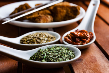 CLOSE UP OF SPOONS WITH SPICES AND CHICKEN NUGGETS ON WOOD BACKGROUND
