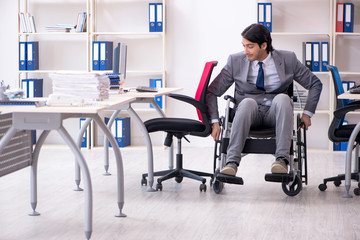 Young handsome employee in wheelchair working in the office  