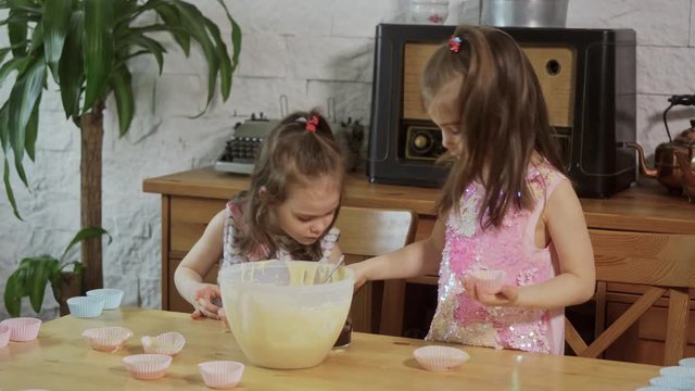 two little adorable girls put cream on the molds to make cupcakes