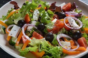 Greek salad with fresh cucumber, cherry tomatoes, sweet pepper, lettuce, red onion, olives and olive oil on dark wooden rustic background. Healthy food concept